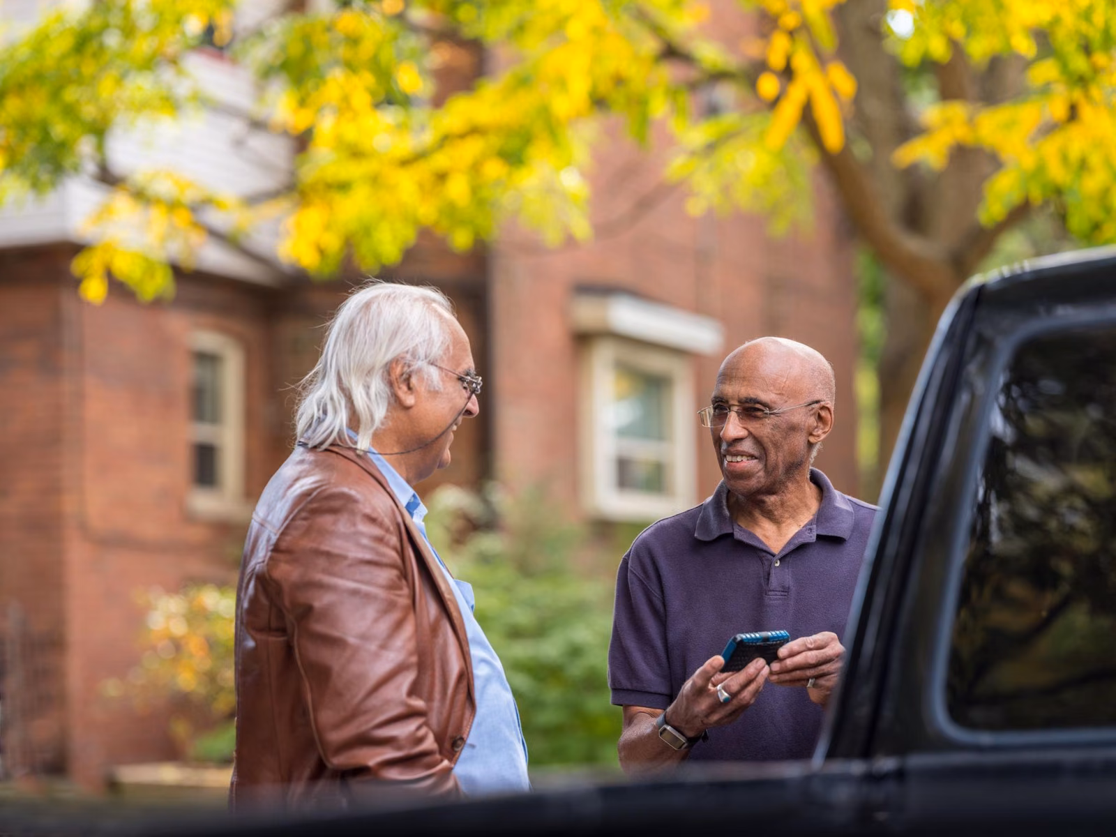Two neighbors talking beside a pickup truck, one holding a phone with the app open